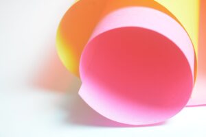 A vibrant abstract composition featuring rolled pink and yellow paper with soft lighting.