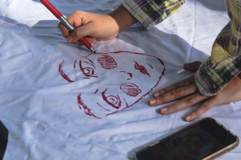 Close-up of hands sketching a face on fabric outdoors in Culiacán Rosales, Mexico.