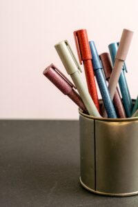 A collection of colorful ballpoint pens in a metallic holder on a desk.